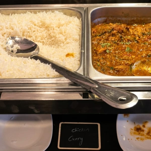 Buffet with white rice and chicken curry in metal serving dishes, with a "chicken curry" sign.